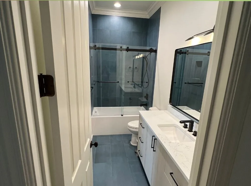 The same bathroom after renovation, with blue tile, a glass shower door and a new vanity