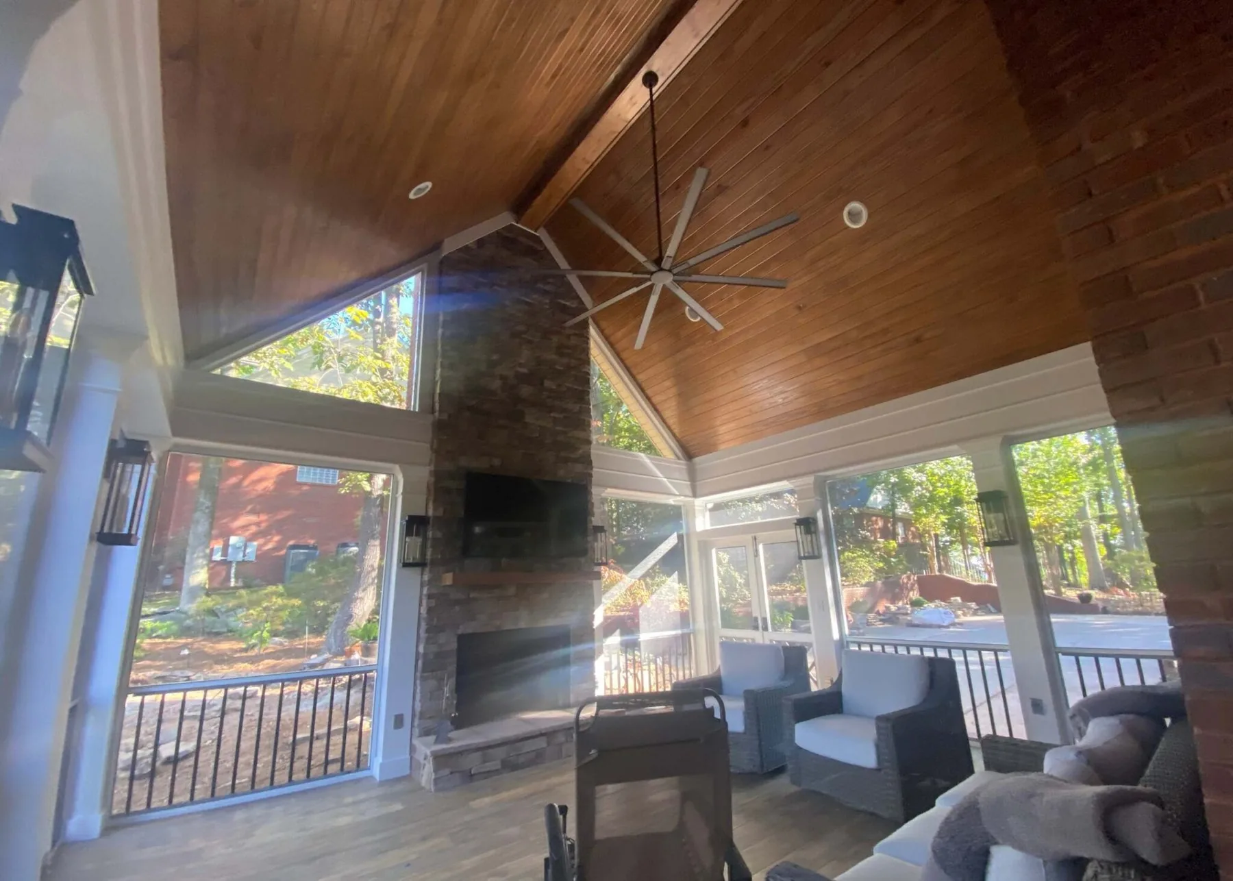 Covered outdoor living space with a wood plank ceiling, a stone fireplace and a ceiling fan