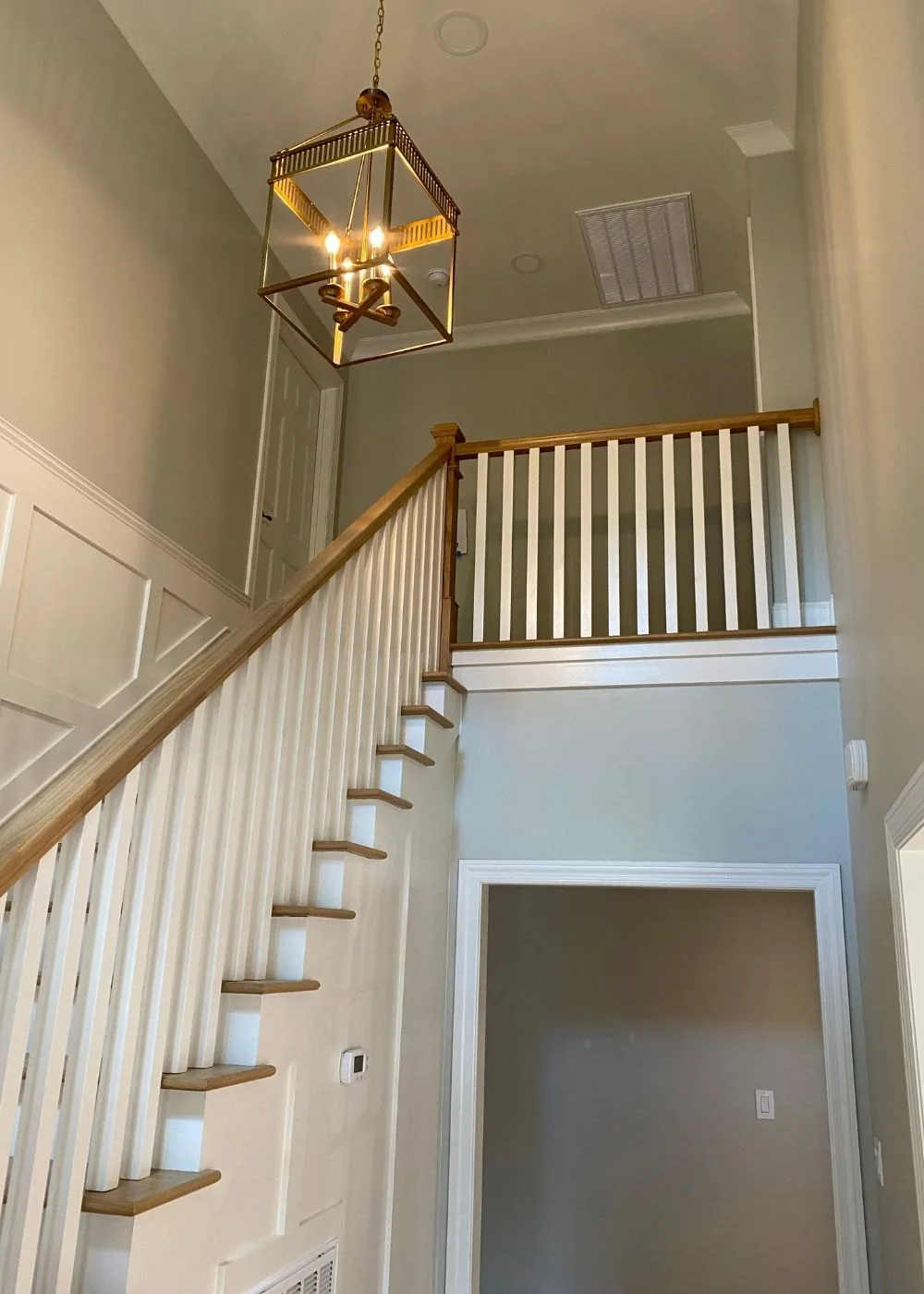 Entry stair with white balusters, a stained handrail and a lantern pendant